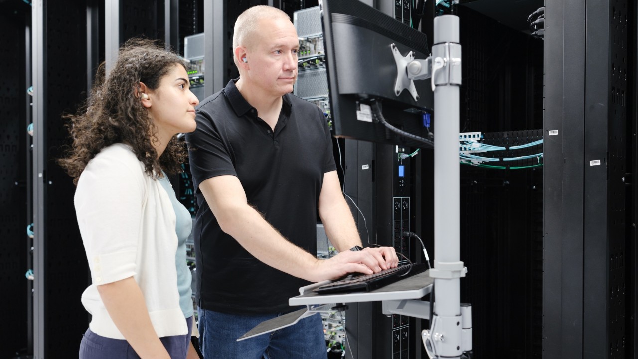 An image of two people working on a computer inside a data center.